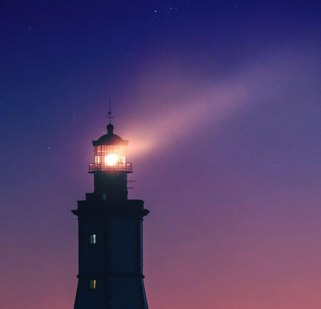 Lit lighthouse beneath a star-filled sky.
