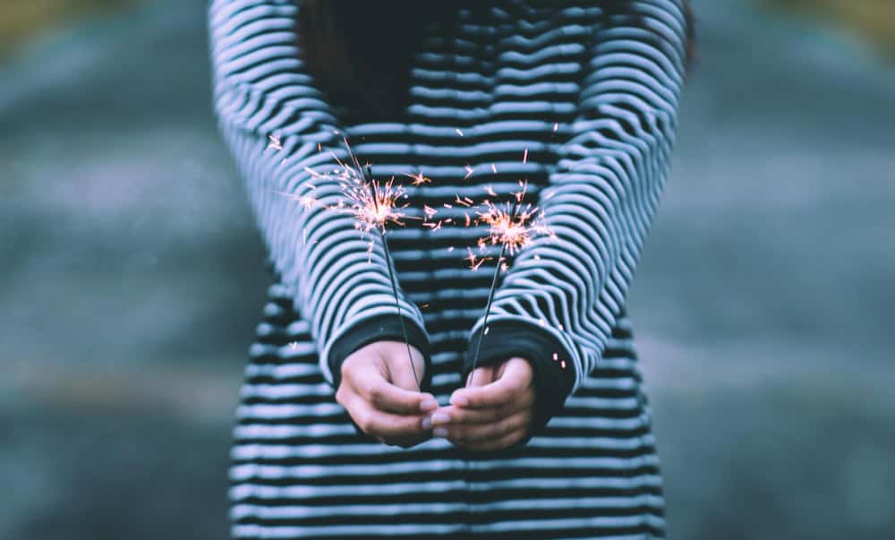 Brightly lit sparklers held by a person in a black and white striped hoodie, symbolizing hope, new beginnings, and emotional healing in counselling.