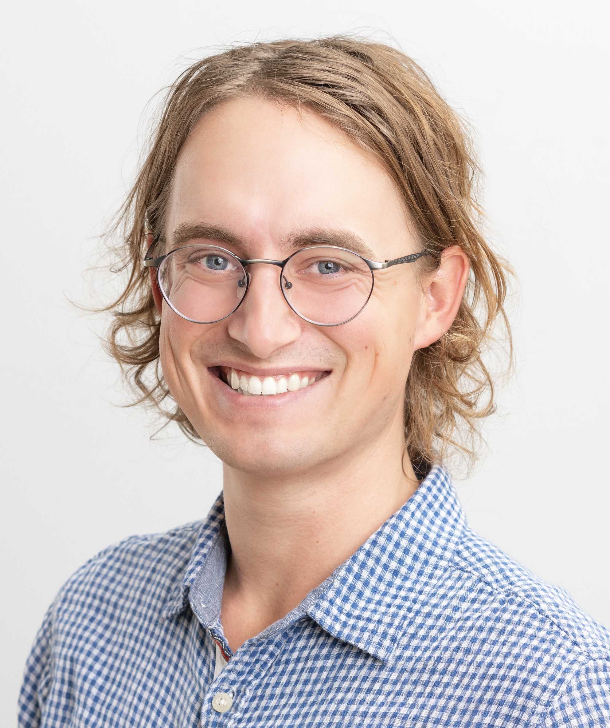 Therapist from Wellspring Counselling smiling, wearing glasses and a blue checkered shirt, representing the compassionate and experienced mental health professionals in our team.