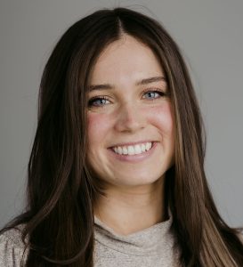 Friendly young woman with long brown hair and bright blue eyes smiling, representing mental health support and counselling services in Vancouver, BC.