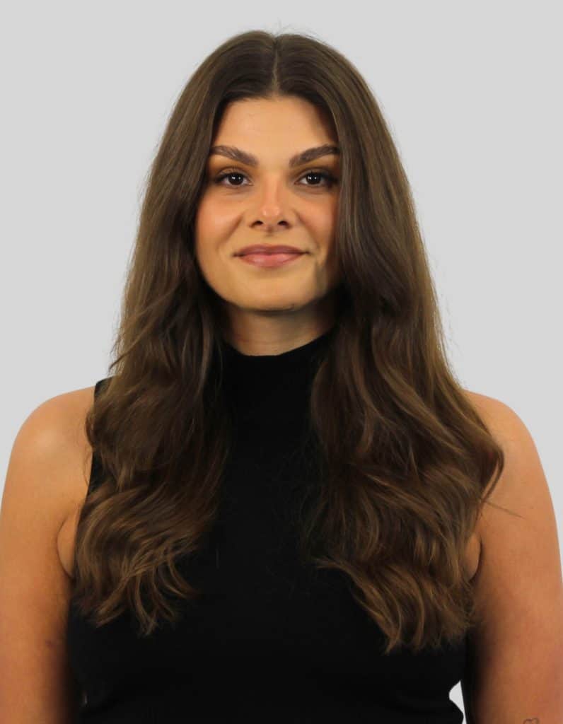 Professional portrait of a woman with long brown hair, wearing a black sleeveless top, smiling softly against a neutral background.