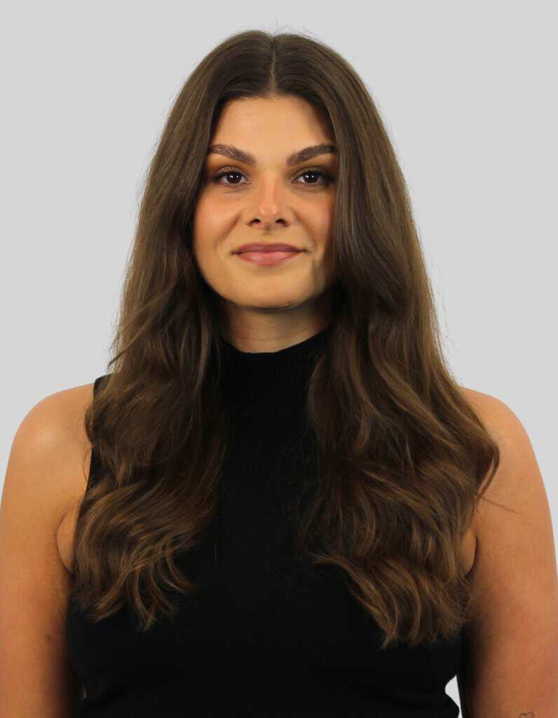 Professional portrait of a woman with long brown hair, wearing a black sleeveless top, smiling softly against a neutral background.