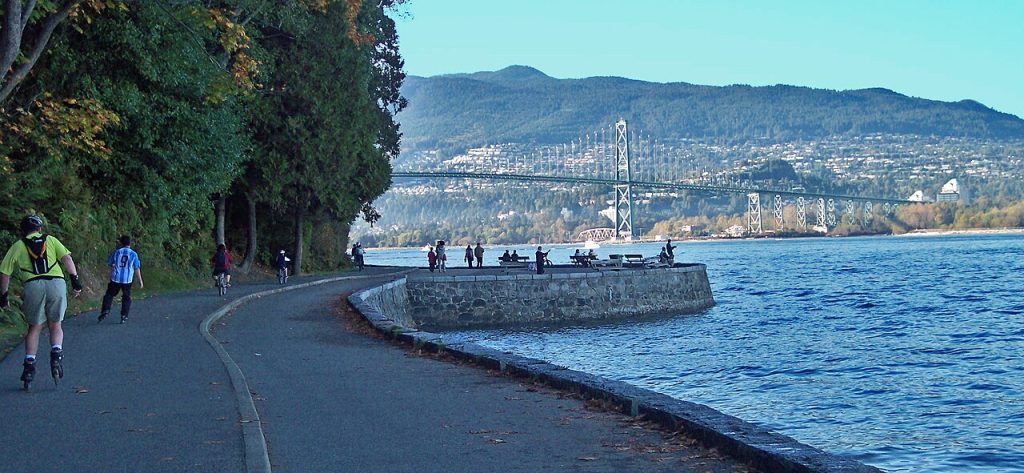 Stanley Park seawall curving beside the water and trees, with Lions Gate Bridge in Vancouver.
